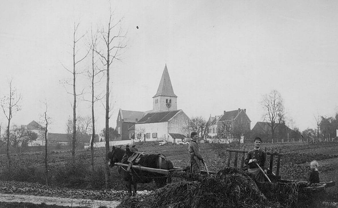 Au centre, l'église Saint-Clément en partie masquée par la ferme Penninckx. A droite, l'écurie de la ferme de Wezembeke transformée en école et, à sa gauche, le bâtiment construit en 1875 pour l'agrandir - Photo IRPA, vers 1900
